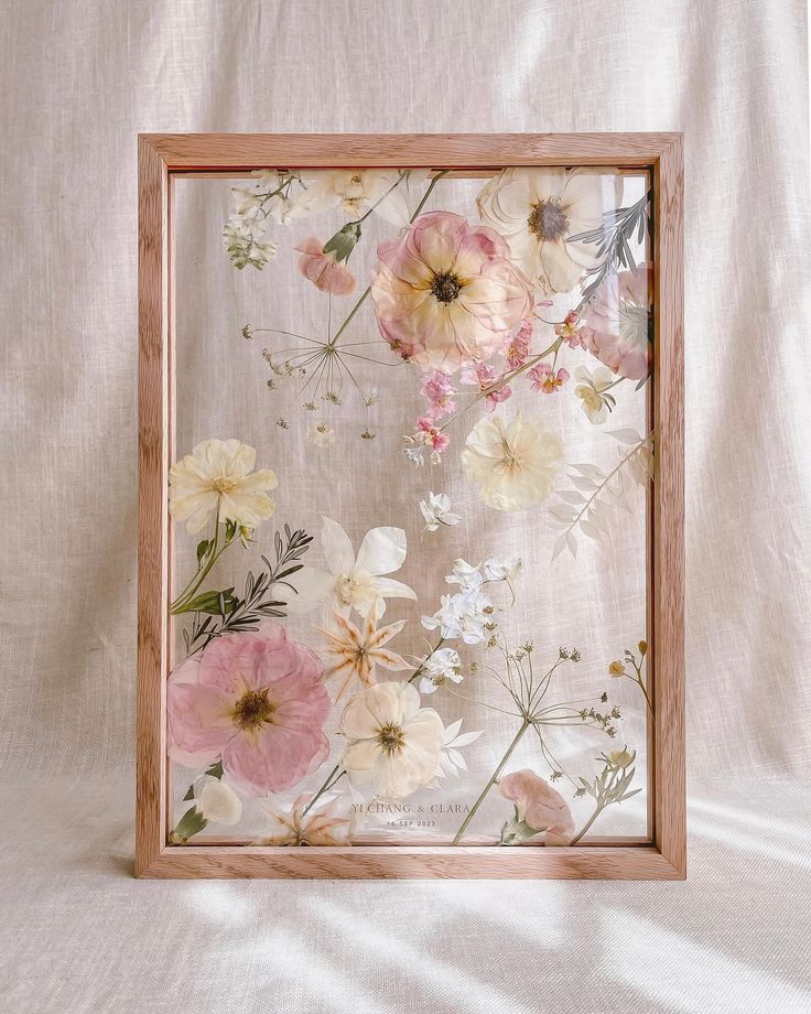 a wooden frame with flowers in it on a white cloth covered background and the image is framed