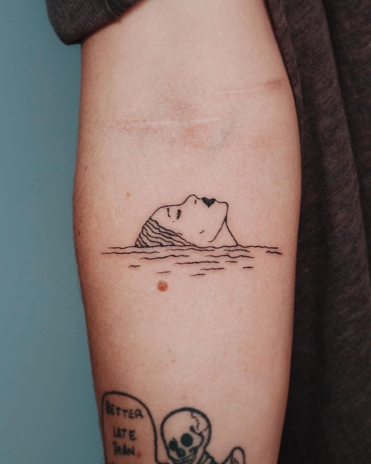 a person with a tattoo on their arm that has a skull in the water and an iceberg behind it