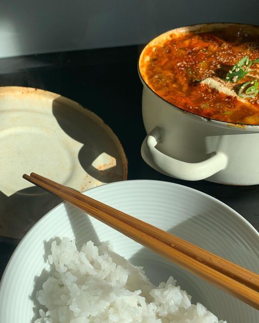 rice and chopsticks sit on a table next to a pot of stew