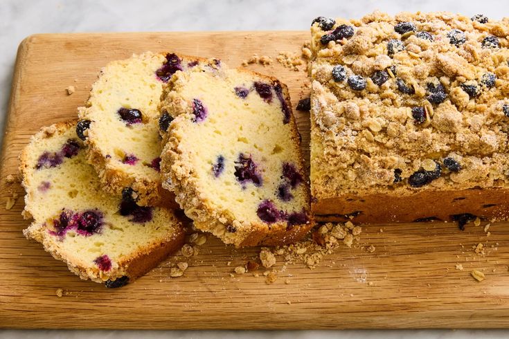 sliced blueberry bread sitting on top of a wooden cutting board next to slices of cake