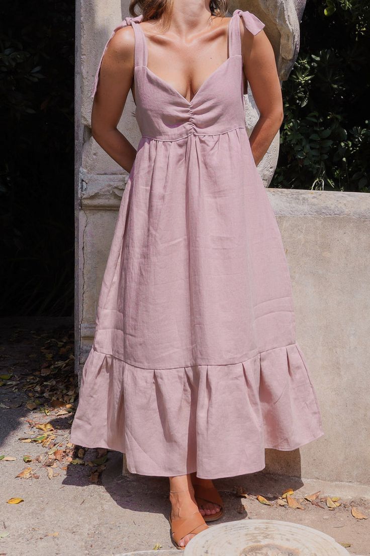 a woman in a pink dress standing next to a stone statue with her eyes closed