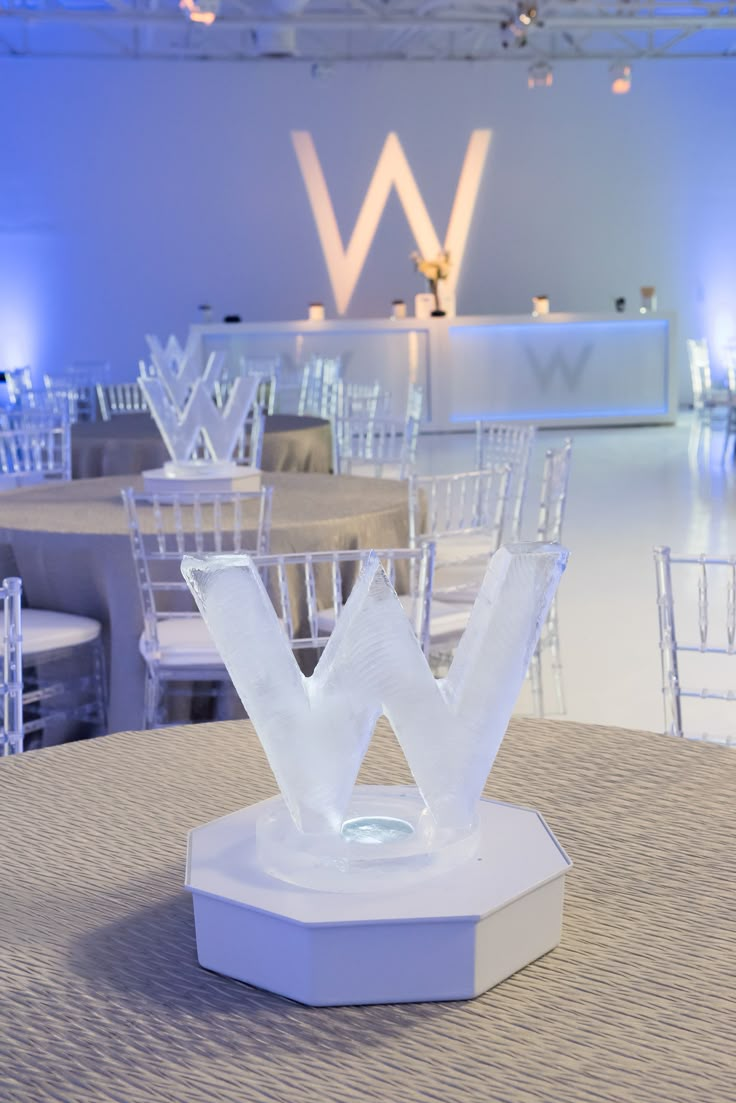 the table is set up for an event with white chairs and round tables in the background