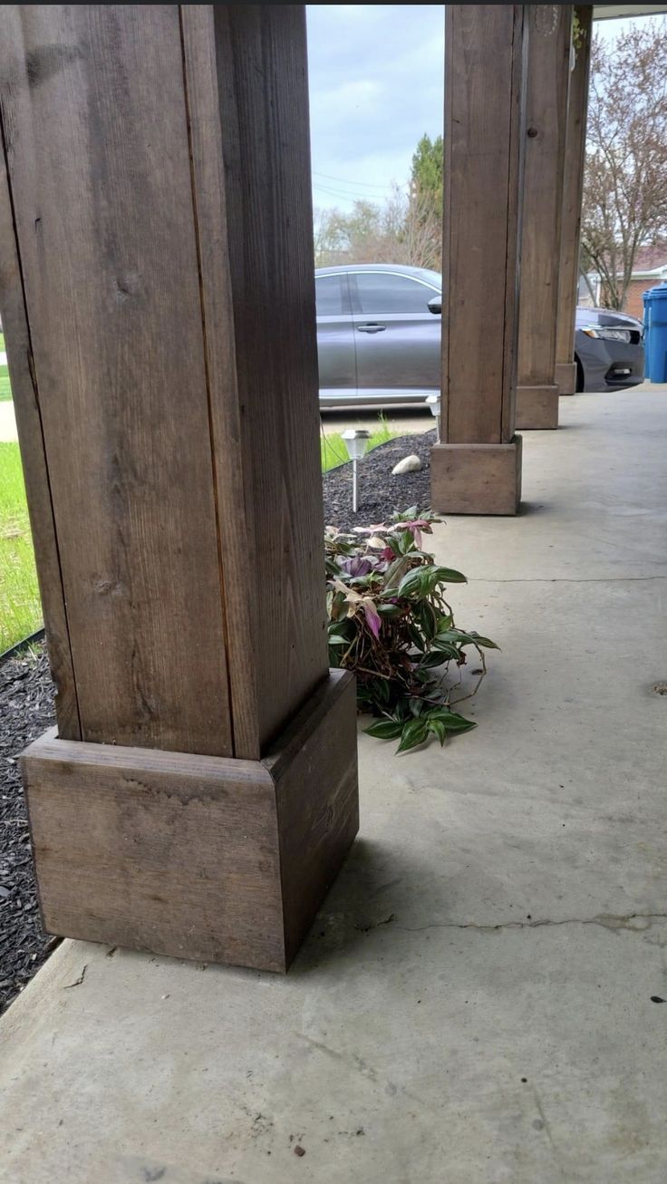 two wooden pillars sitting on top of a cement floor next to grass and flowers in front of a car