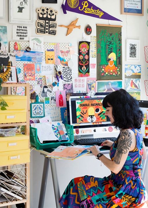 a woman sitting at a desk with lots of art on the wall behind her and writing