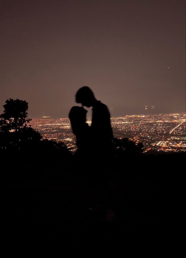 the silhouette of two people in front of a cityscape at night with lights on