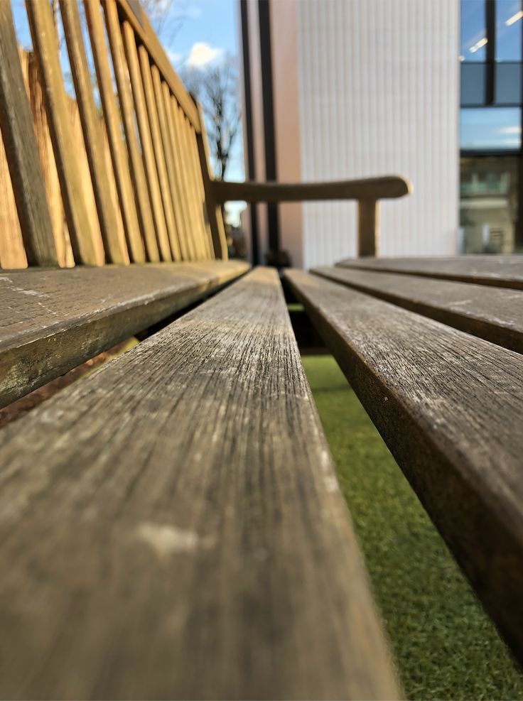 two wooden benches sitting next to each other in front of a building with grass on the ground