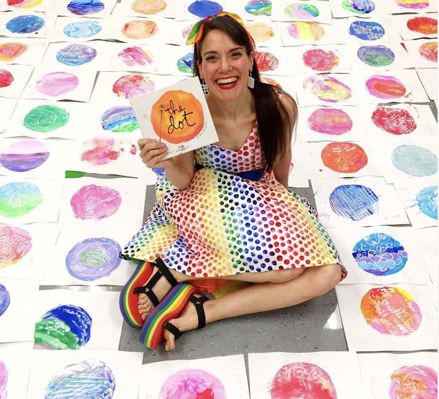 a woman sitting on the ground holding up a sign that says, happy art with lots of circles in the background