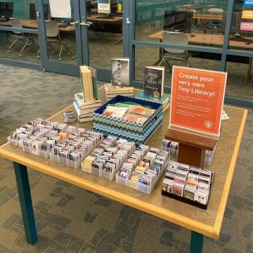 there is a table with many books on it and an orange sign that says create your own library