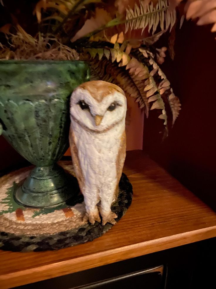 an owl figurine sitting on top of a green vase next to a fern