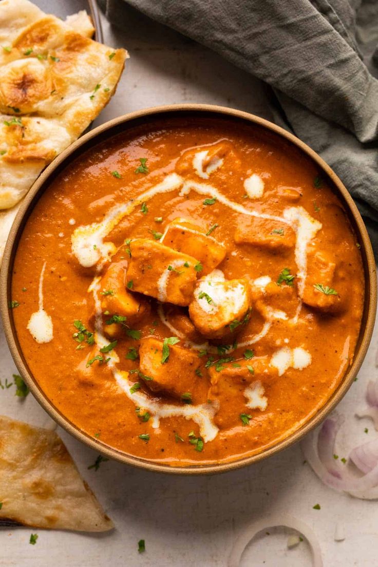 a bowl filled with red curry next to bread and pita bread on the side