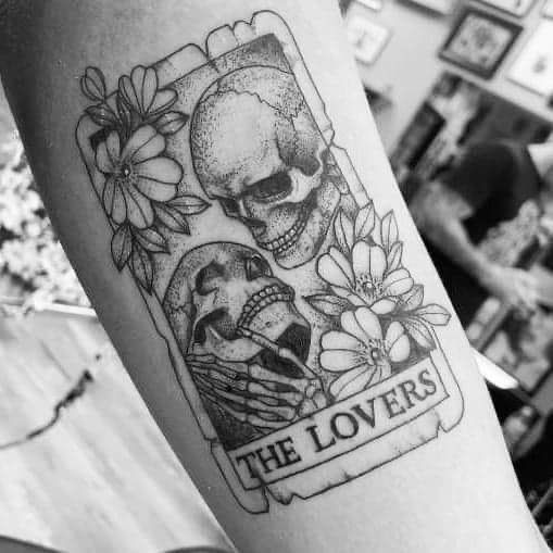 a black and white photo of a skull with flowers on it's arm that says the lovers