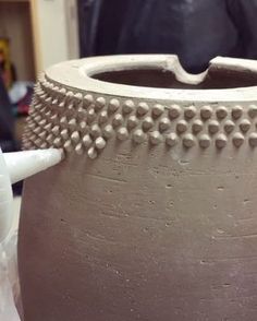 a clay pot with rivets on it and a person in the back ground