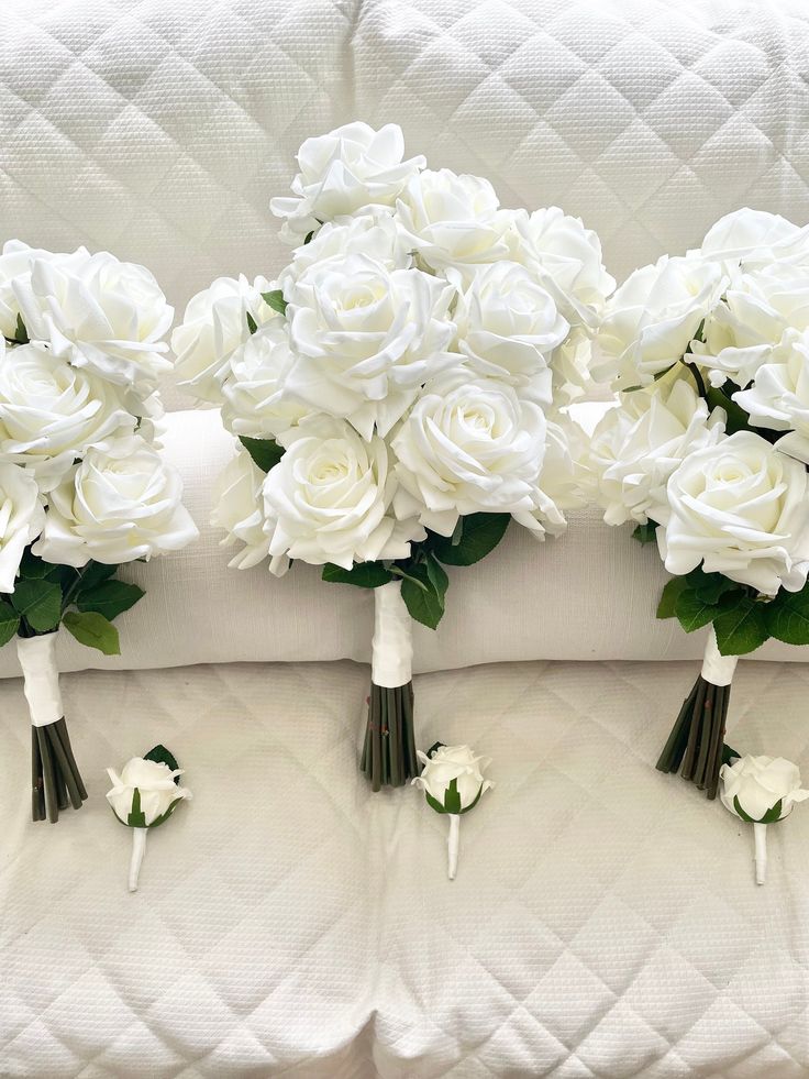 three bouquets of white roses are arranged on the back of a couch in front of pillows