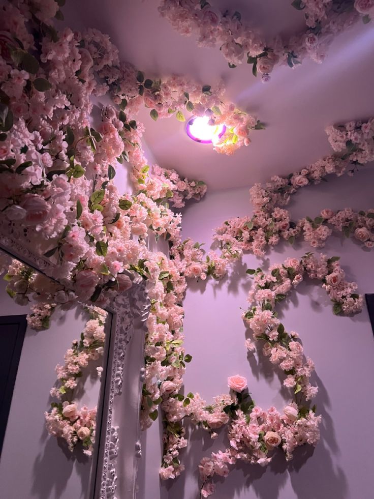 pink flowers are growing on the wall next to a mirror and light fixture in a room with white walls