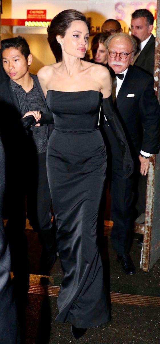 a woman in a black dress is walking down the street with other people behind her