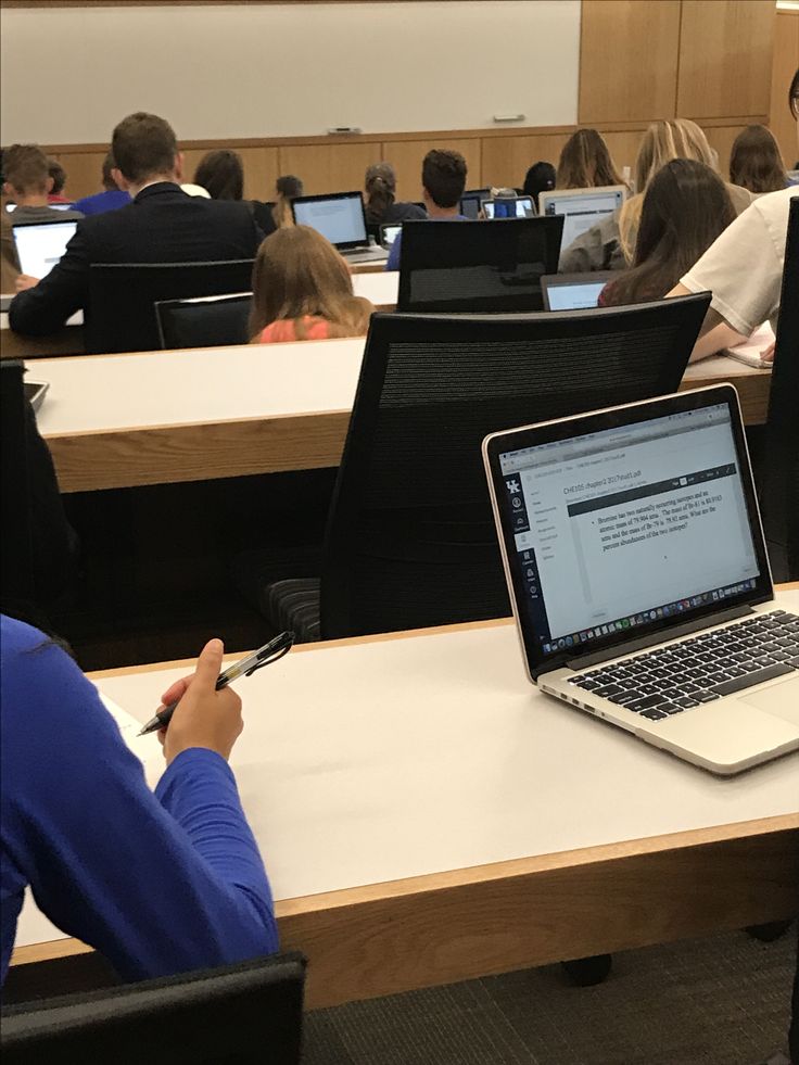 people sitting at desks with laptop computers in front of them and one person writing