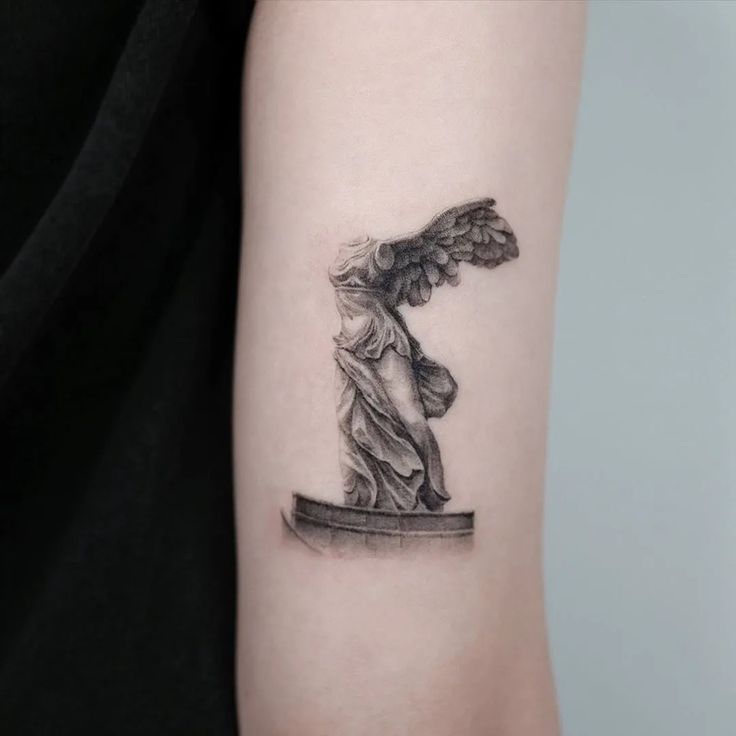 a woman's arm with an angel statue tattoo on the left side of her arm