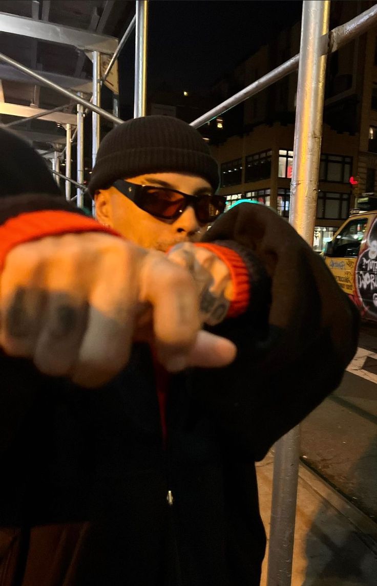 a man pointing at the camera while wearing sunglasses and a beanie on his head