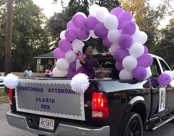 a truck with balloons in the back and a woman on the bed waving to people