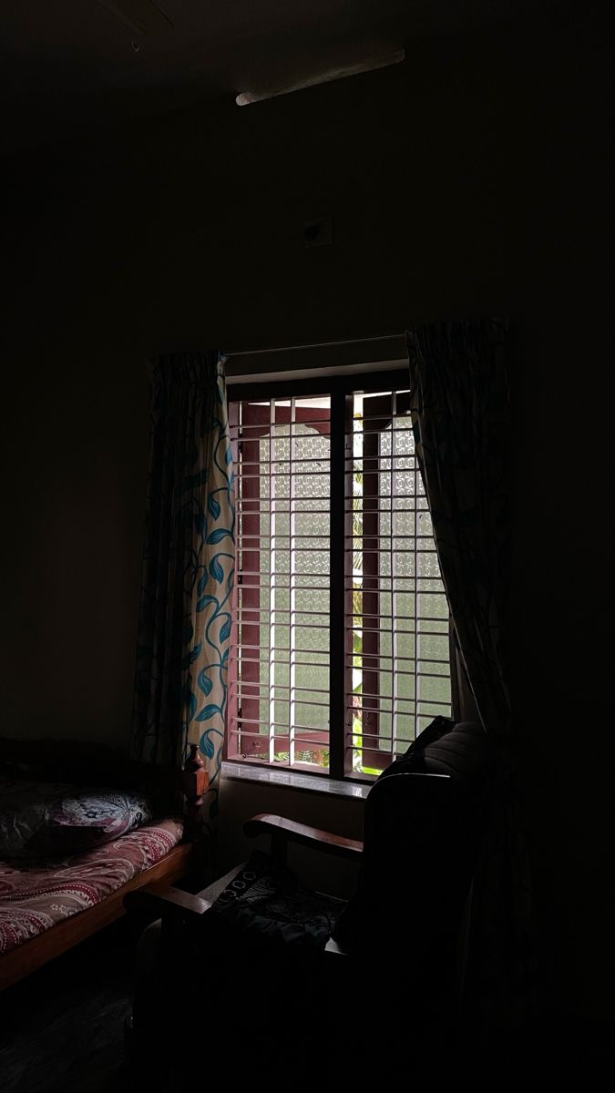 a dark room with a bed, chair and window in the corner that has blinds on it