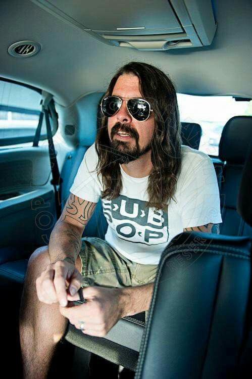 a man with long hair and sunglasses sitting in the back seat of a car looking at his cell phone