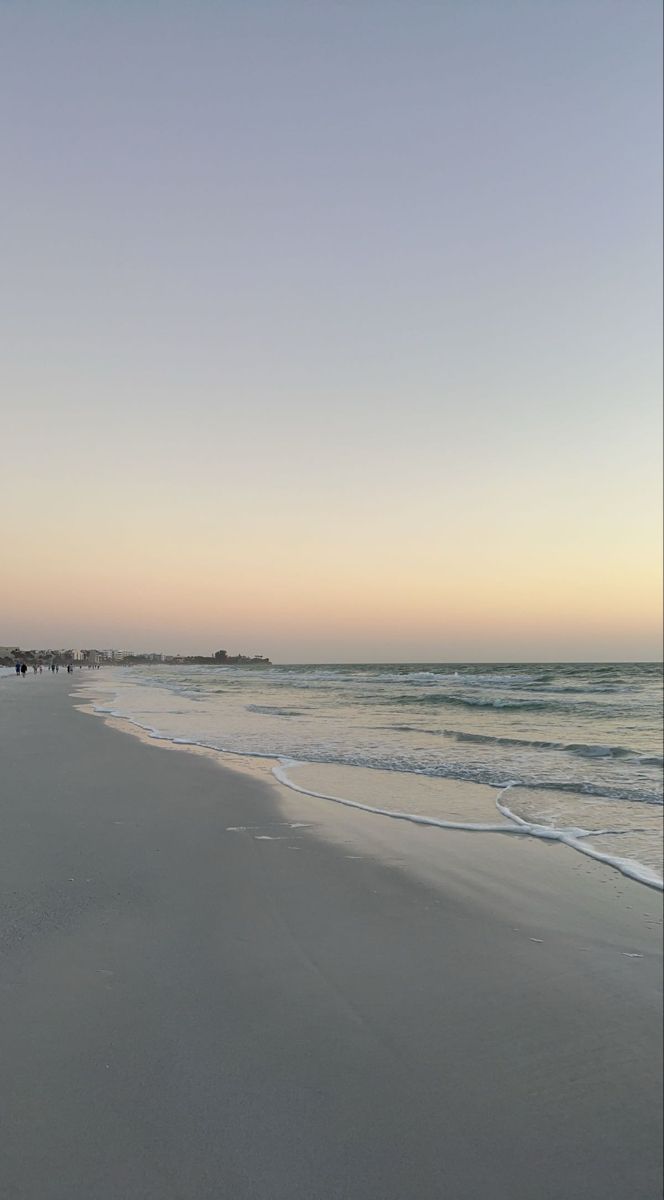 people are walking along the beach at sunset