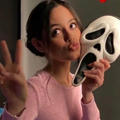 a woman holding up a fake mask to her face and making the peace sign with her hand