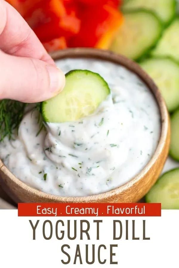 a hand dipping a cucumber into a bowl of yogurt dill sauce