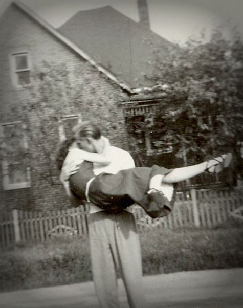 an old black and white photo of a man holding a woman on his back in front of a house