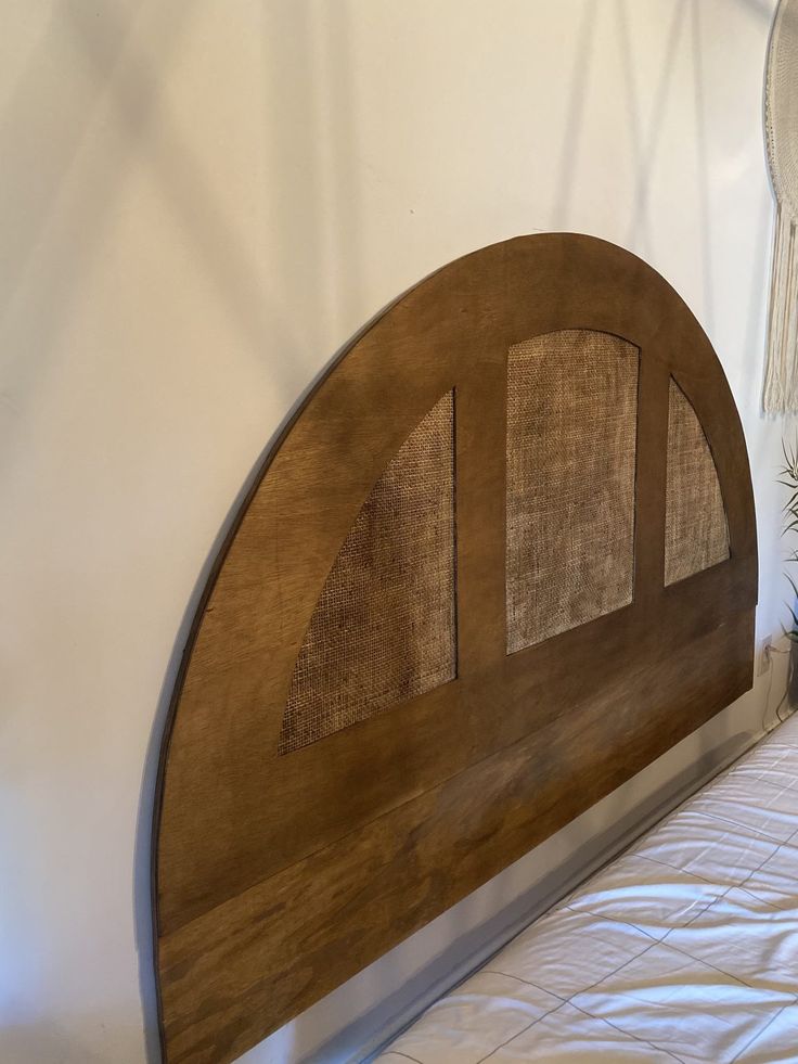 a wooden bed headboard sitting on top of a white sheet covered floor next to a plant