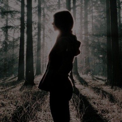 a woman standing in the woods with her back to the camera, looking at trees