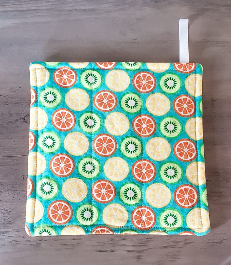 an orange and kiwi pattern on a teal colored cloth with white string hanging from it