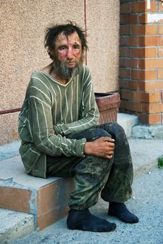 a man with long hair and beard sitting on the steps in front of a building