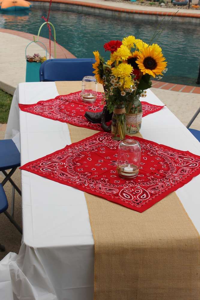 the table is set with sunflowers and mason jars on it, along with a red bandana