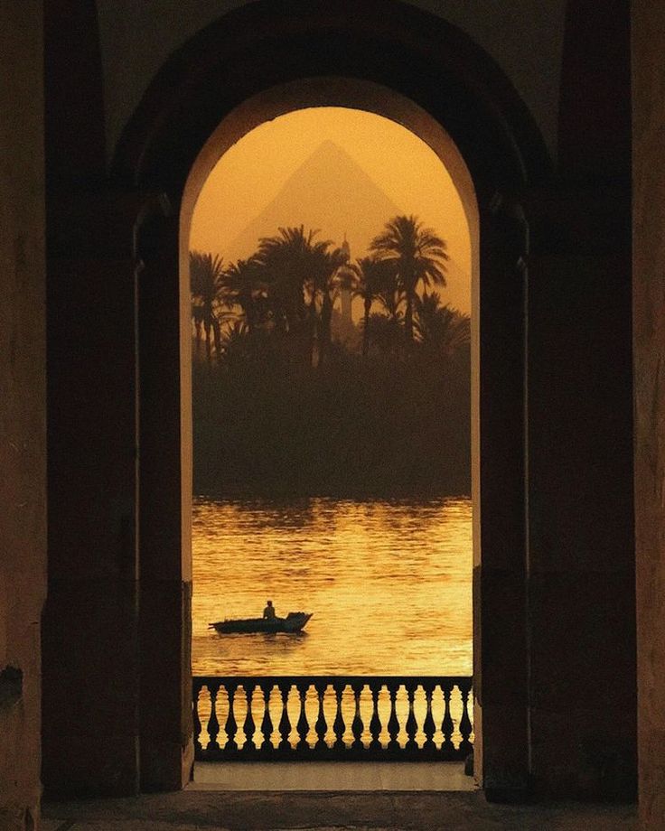 a man in a boat is seen through an archway to the water with palm trees