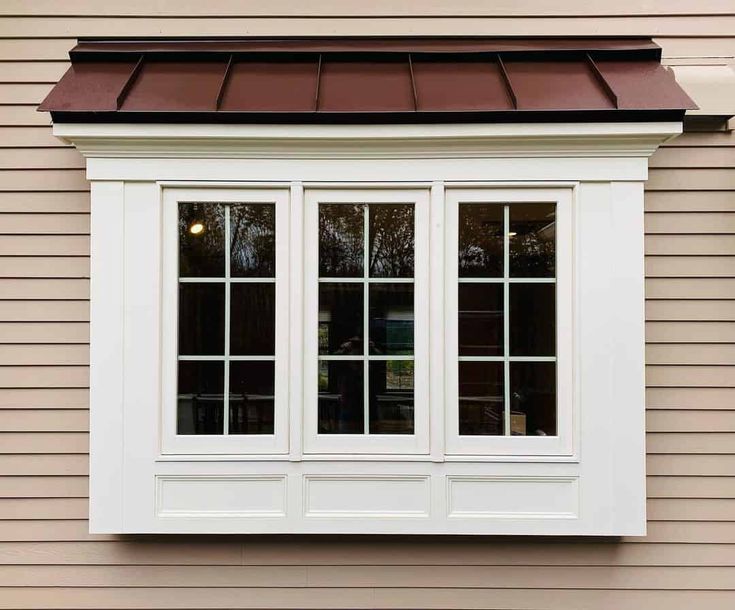 a white window on the side of a house with brown shingles and a red roof