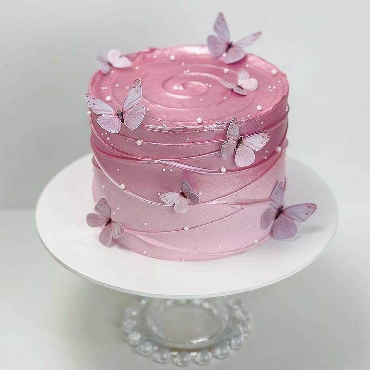 a pink cake with butterflies on it sitting on top of a white platter,