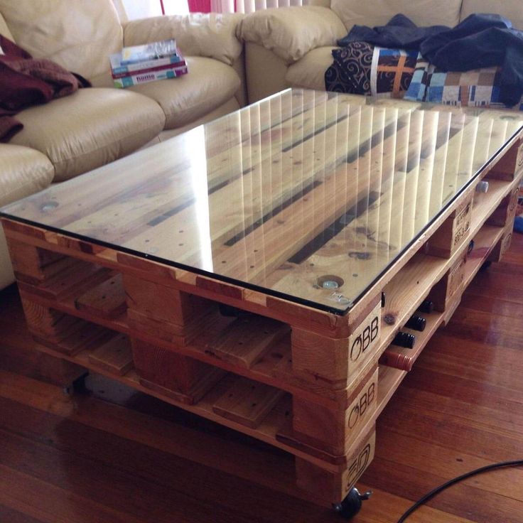 a coffee table made out of pallet wood with glass top and wheels on the bottom