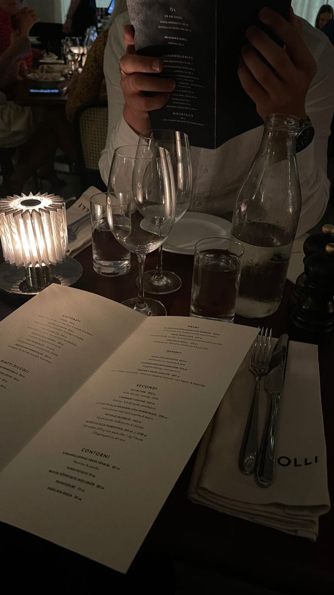 a person is sitting at a table with wine glasses and an open menu in front of them