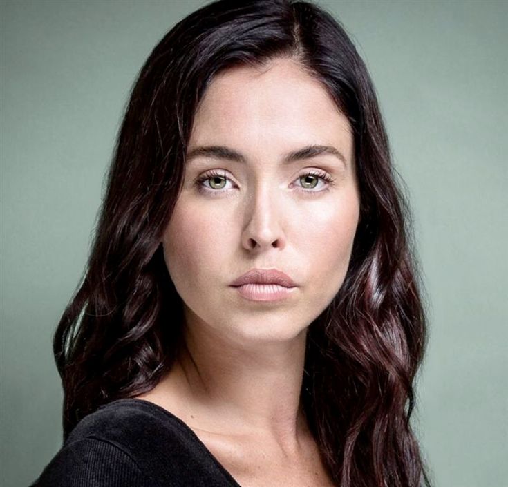 a woman with long dark hair is looking at the camera while wearing a black top