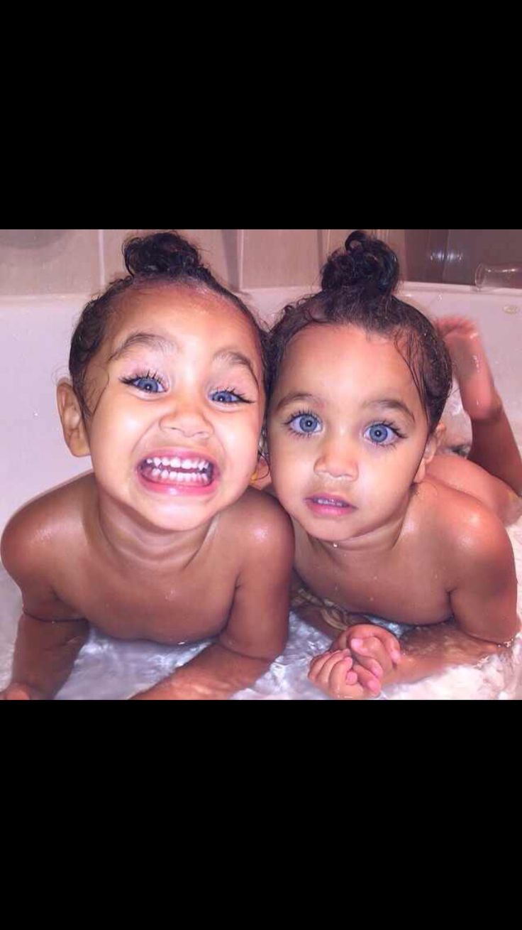 two young children laying in a bathtub with their heads turned to the side and smiling