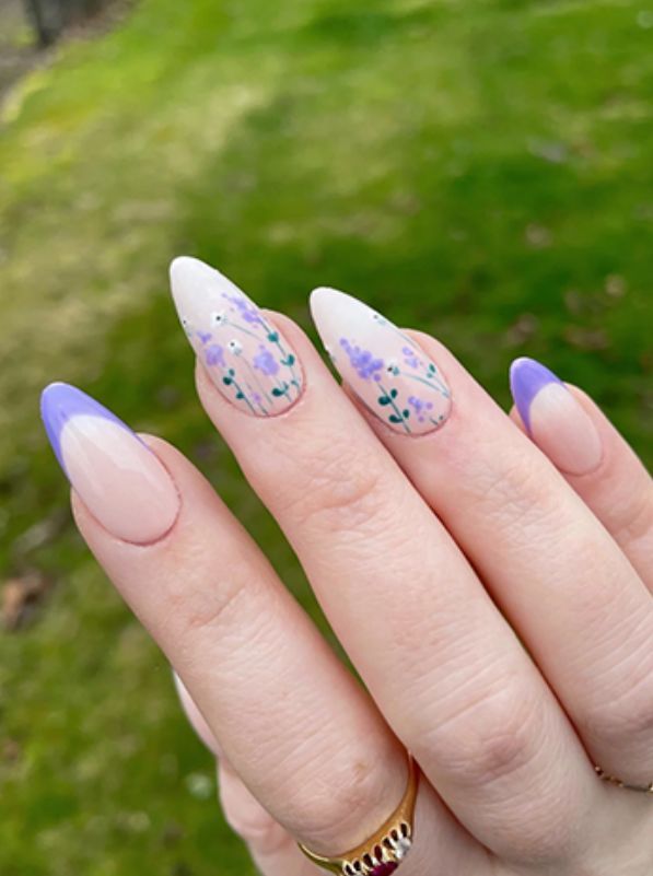 Almond-shaped nails with a clear base, adorned with delicate lavender flower accents and soft pastel purple tips, perfect for a fresh spring look. Nails With Lavender Flowers, Lavender Flower Nail Designs, Lavender Flower Nail Art, Purple Nails Lavender, Lavender Floral Nails, Grad Nails Purple, Lavender Design Nails, Lavender Acrylic Nails Almond, Cute Spring Nails Acrylic Almond