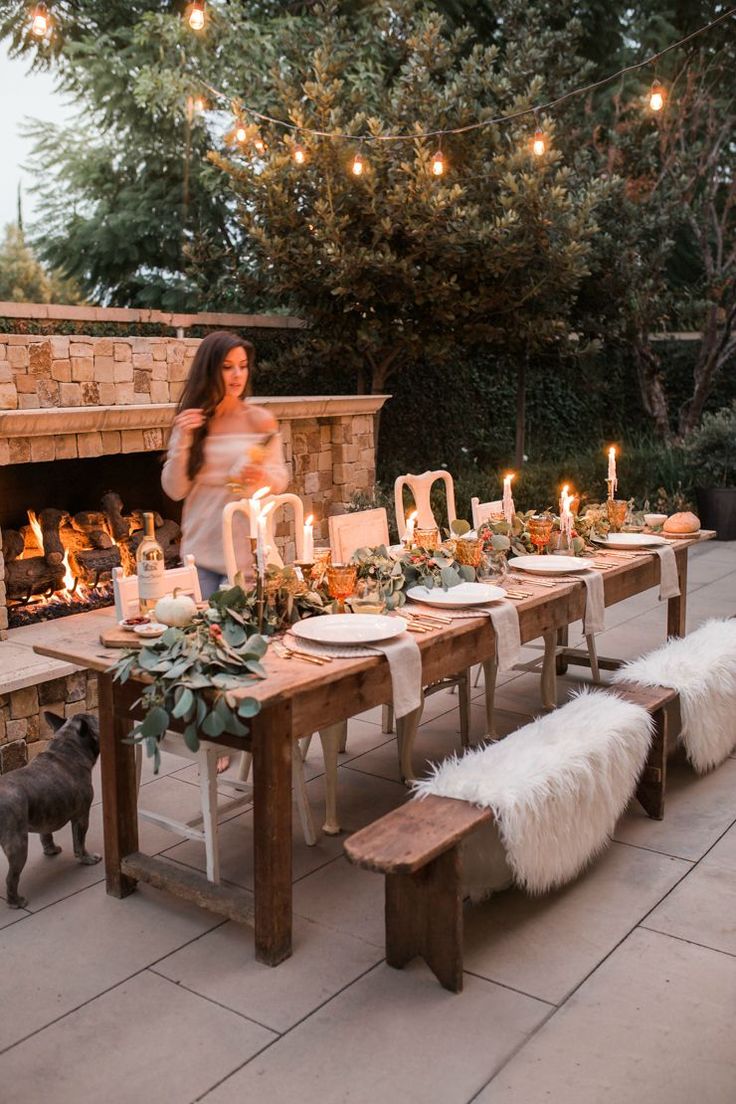 a woman standing in front of a table with candles and plates on it next to a fire place