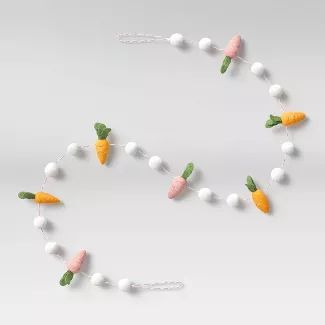 a string of carrots and cotton balls is hanging on a white wall with green leaves