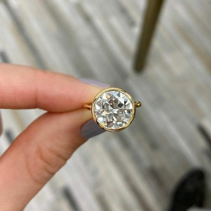 a woman's hand holding a ring with a white diamond in the middle and yellow gold band