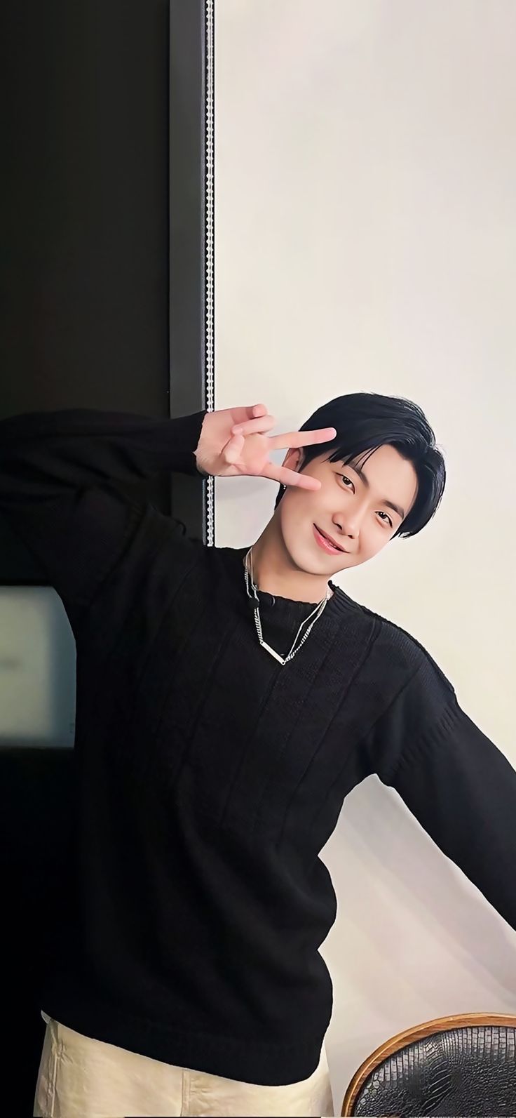 a young man standing next to a chair in front of a wall holding his hand up