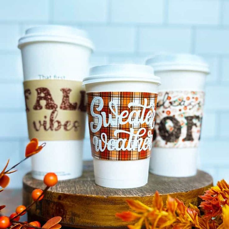 three coffee cups sitting on top of a wooden table next to autumn leaves and pumpkins