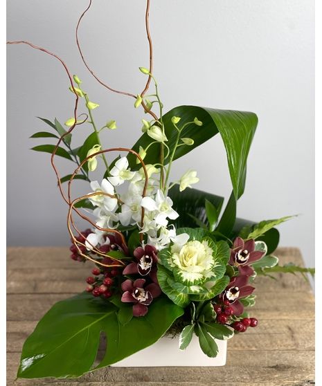 an arrangement of flowers and greenery in a white vase on a wooden table with green leaves