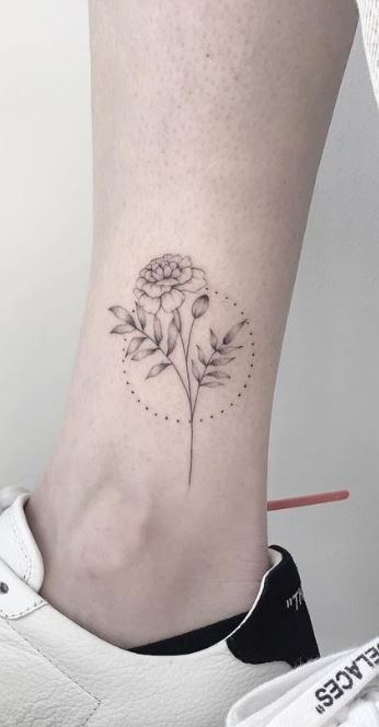 a flower tattoo on the ankle is shown in black and grey ink, with small dots around it