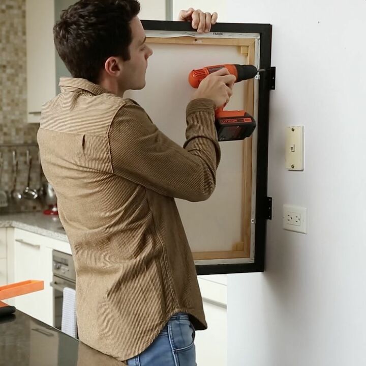 a man is using an electric drill to attach a framed artwork on the wall in his kitchen